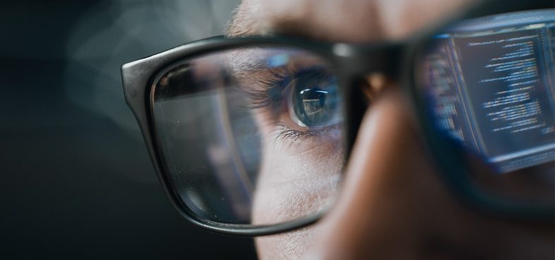 Pictorial representation of Iran cyber attacks. Close-up of a person wearing glasses, with computer code reflected in the lenses.